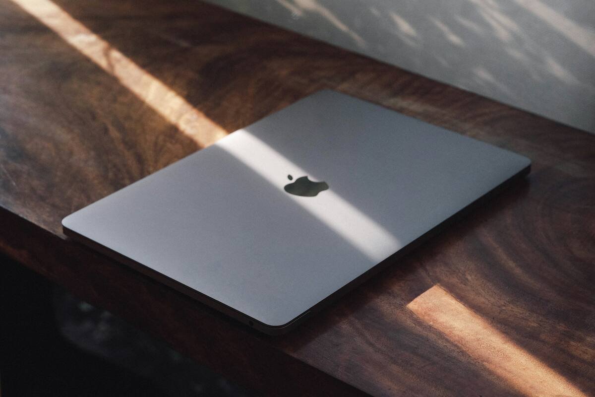 A closed aluminium laptop on a dark wooden desk in a band of late sunlight