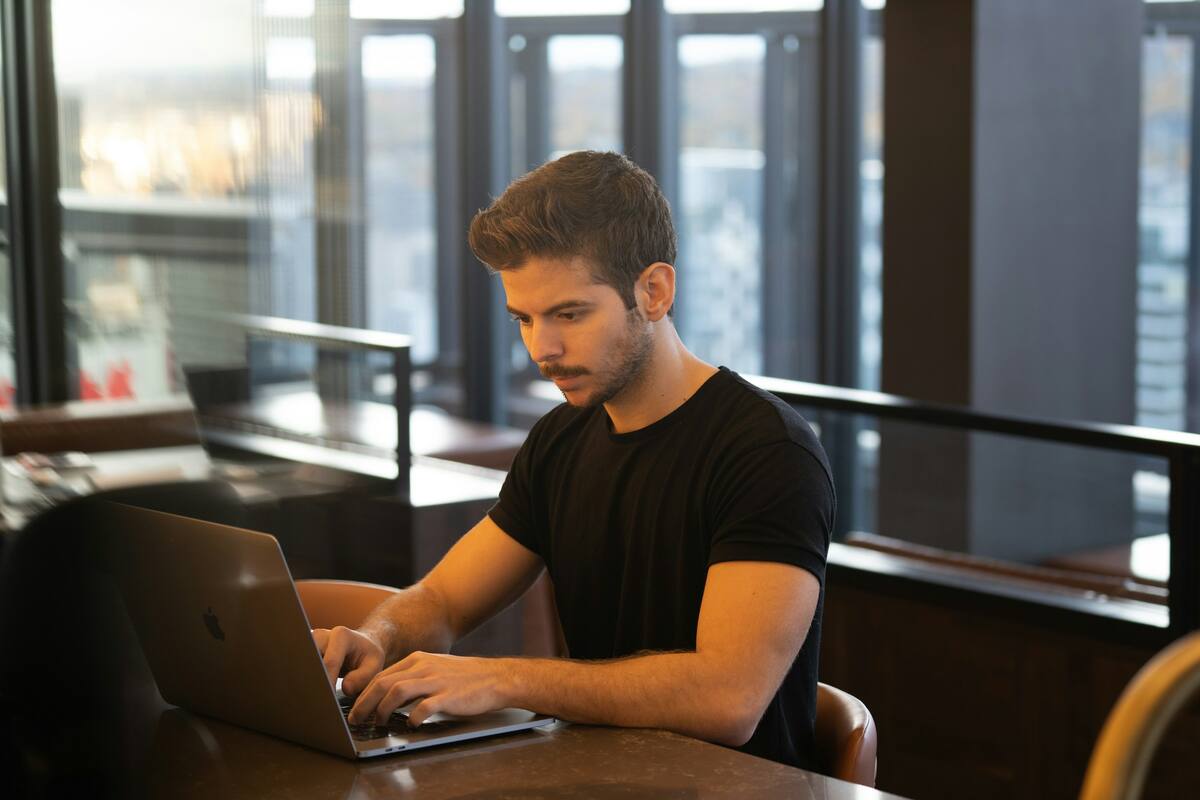A founder working on a laptop at a table by tall windows
