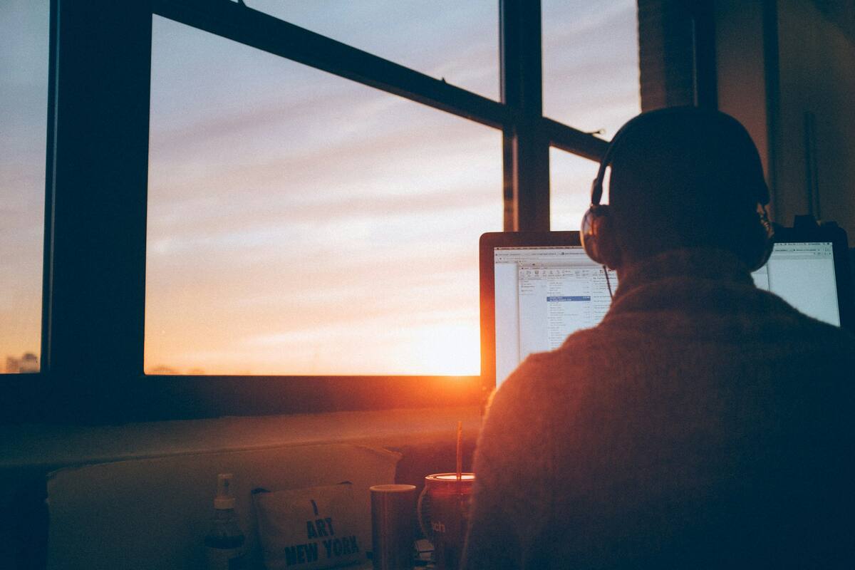 A founder in headphones working at a desk by a window as the sun sets